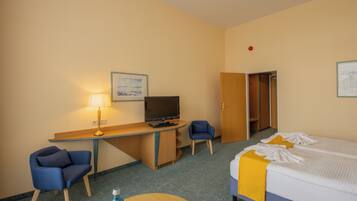 Une chambre d’hôtel comprenant un lit, un bureau avec un ordinateur et une télévision, une chaise et une petite table.