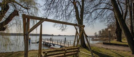 Un conjunto de columpios de madera en un parque, con un lago y un muelle al fondo.
