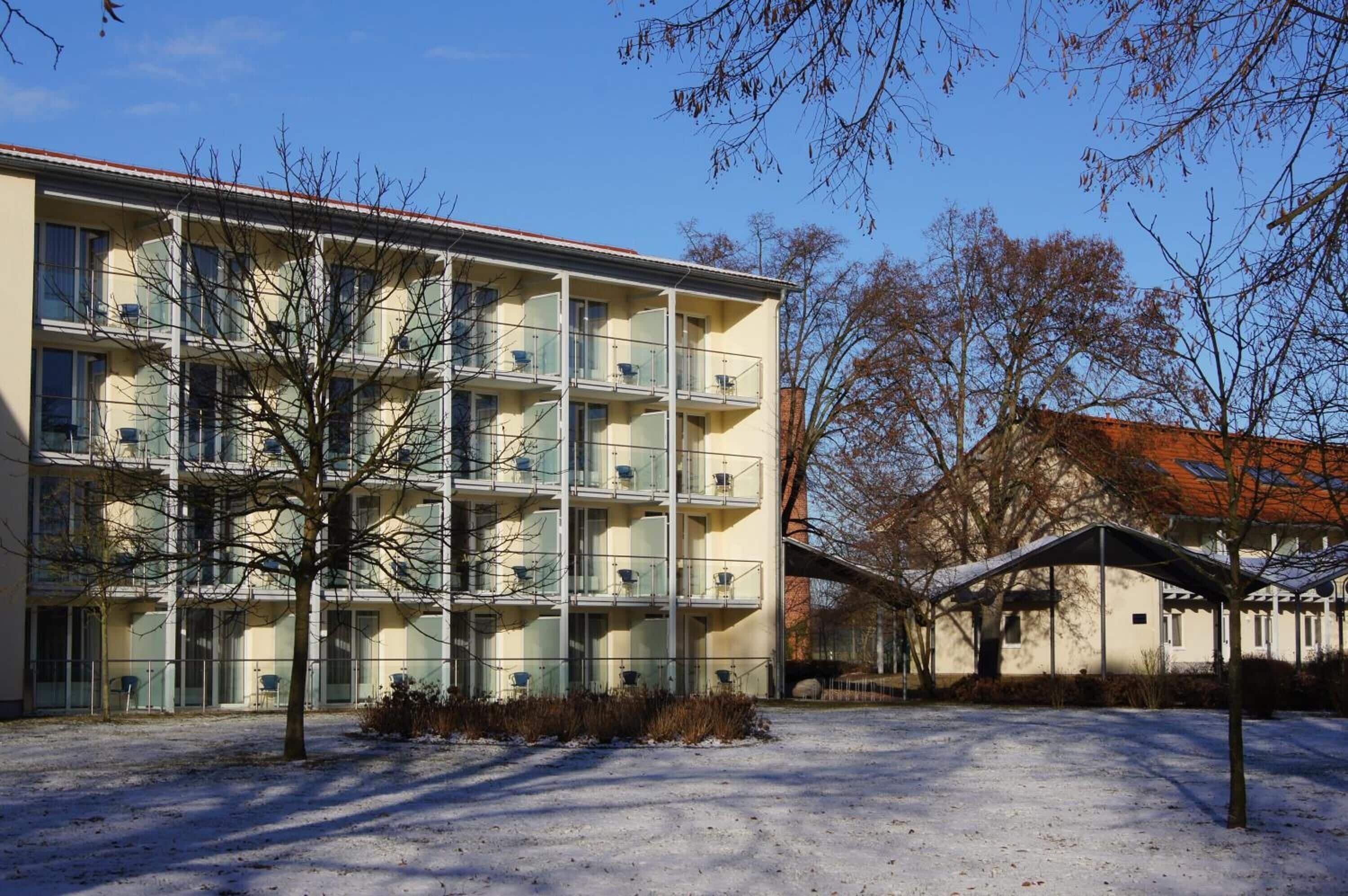 A multi-story building with balconies, a covered parking area, and a snow-covered ground.