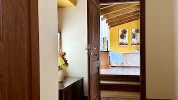 Un couloir avec une porte en bois qui donne sur une chambre à coucher, où se trouvent un lit, une table de chevet et un mur orné de tableaux.