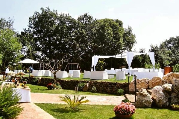 Un salón de bodas al aire libre con carpas blancas, mesas redondas y un muro de piedra.
