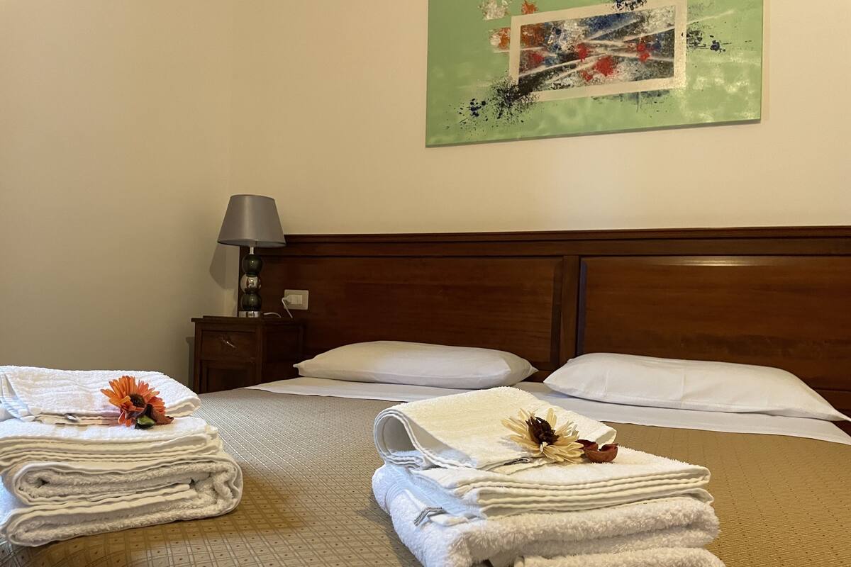 Una habitación de hotel con una cama bien hecha, una mesita de noche con una lámpara y un cuadro en la pared.