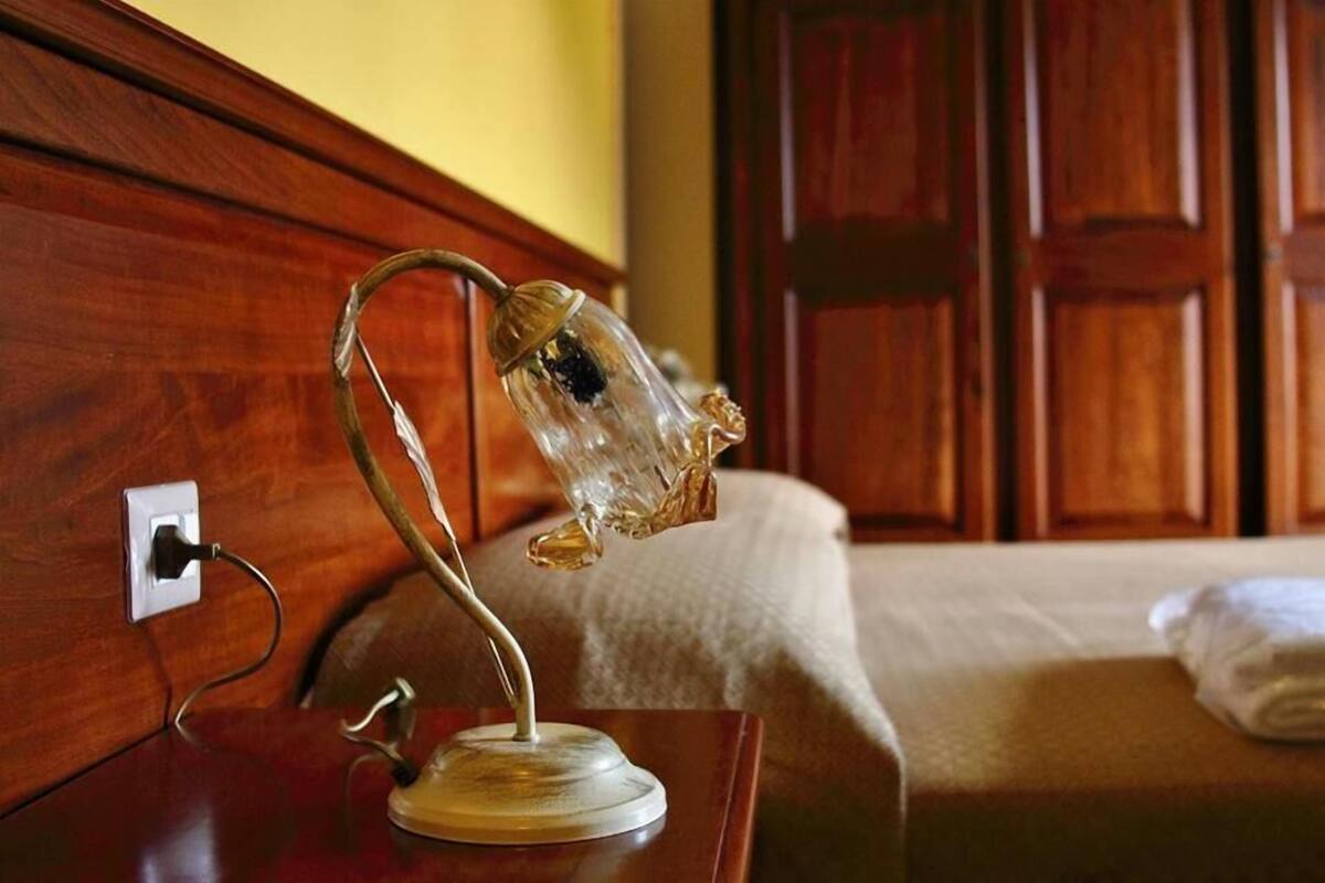 Una habitación con cabecera de madera, lámpara de noche, toma de corriente y una cama bien hecha con una toalla doblada.