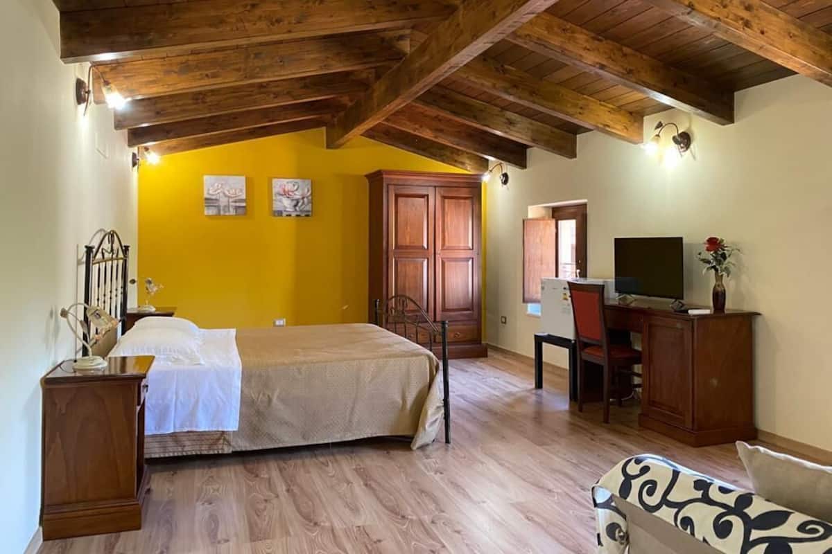 Un dormitorio con una cama, vigas de madera en el techo, un escritorio con silla y un televisor.
