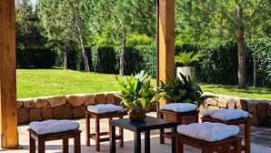 Un patio al aire libre con mesas y sillas de madera, rodeado por un muro de piedra y abundante vegetación.