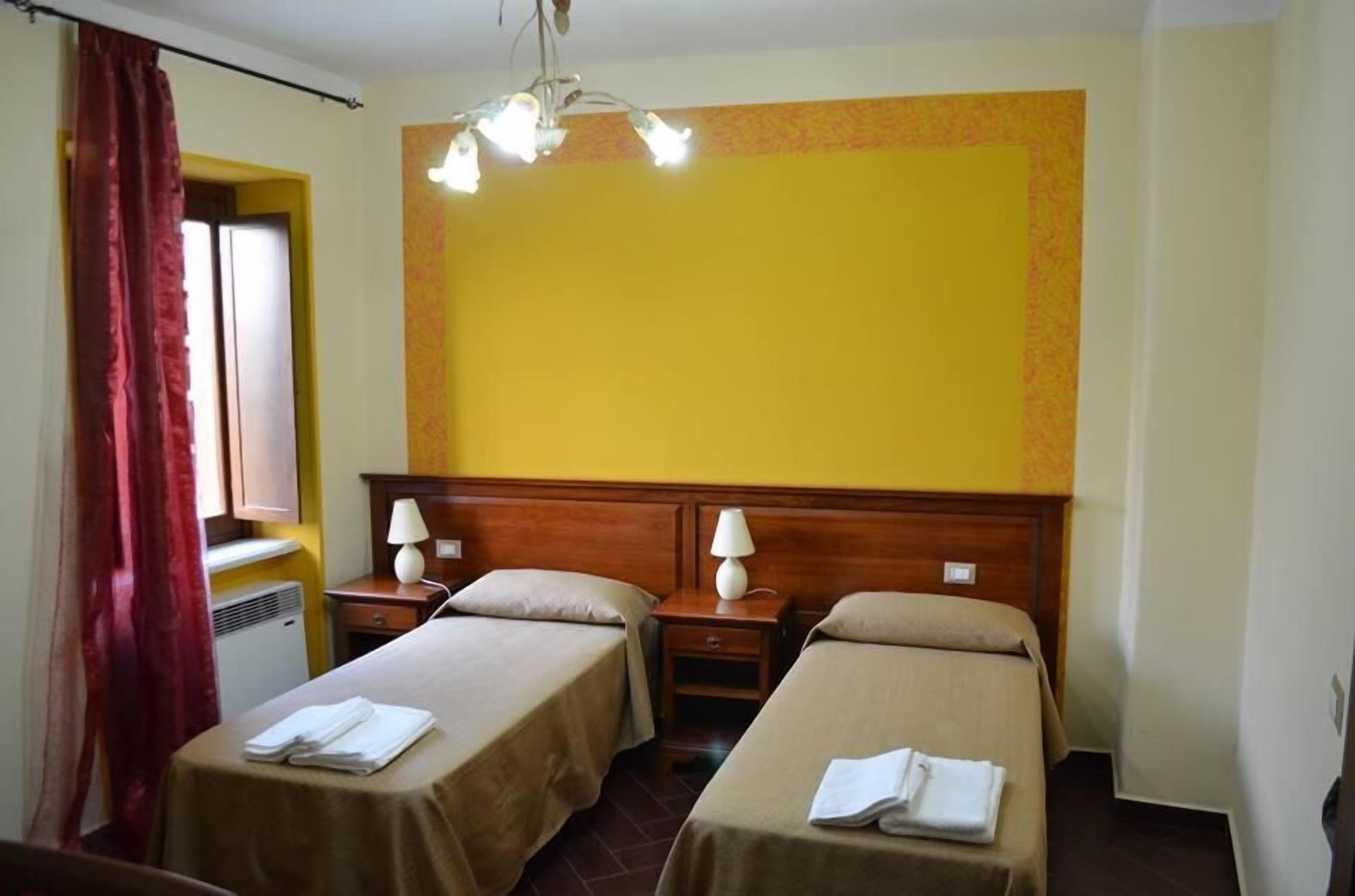 A hotel room with two single beds, a wooden headboard, a ceiling light fixture, and a window with curtains.