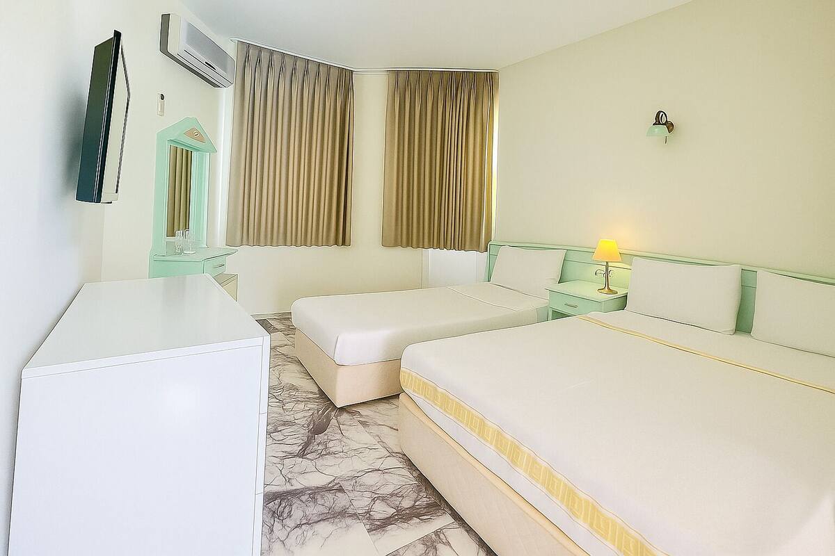 A hotel room with two single beds, a desk, a mirror, a lamp, and a wall-mounted air conditioner.