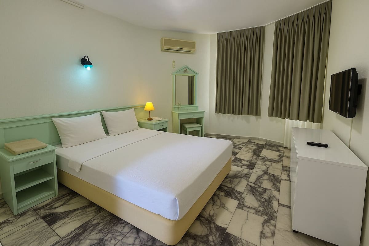 A hotel room with a bed, nightstand, lamp, mirror, and a television on a stand.