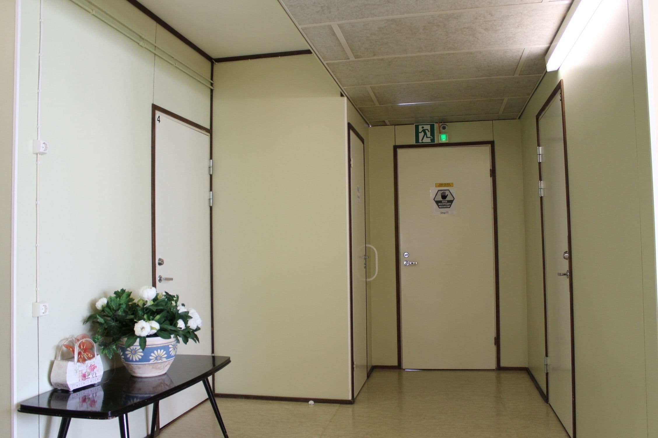 A hallway with a door marked '4', a potted plant, and a small table with a bag and a box.