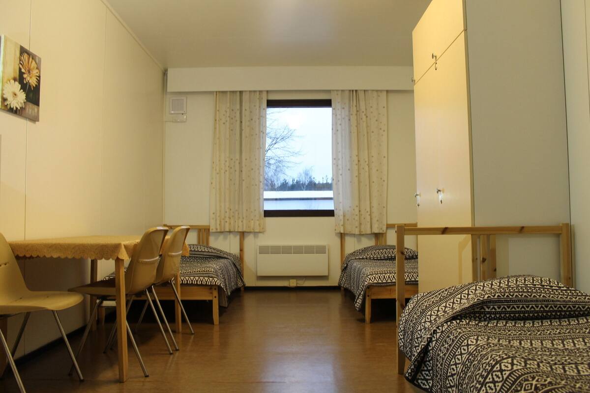 Une chambre de dortoir avec deux lits, un bureau, des chaises, une fenêtre avec des rideaux et un radiateur.