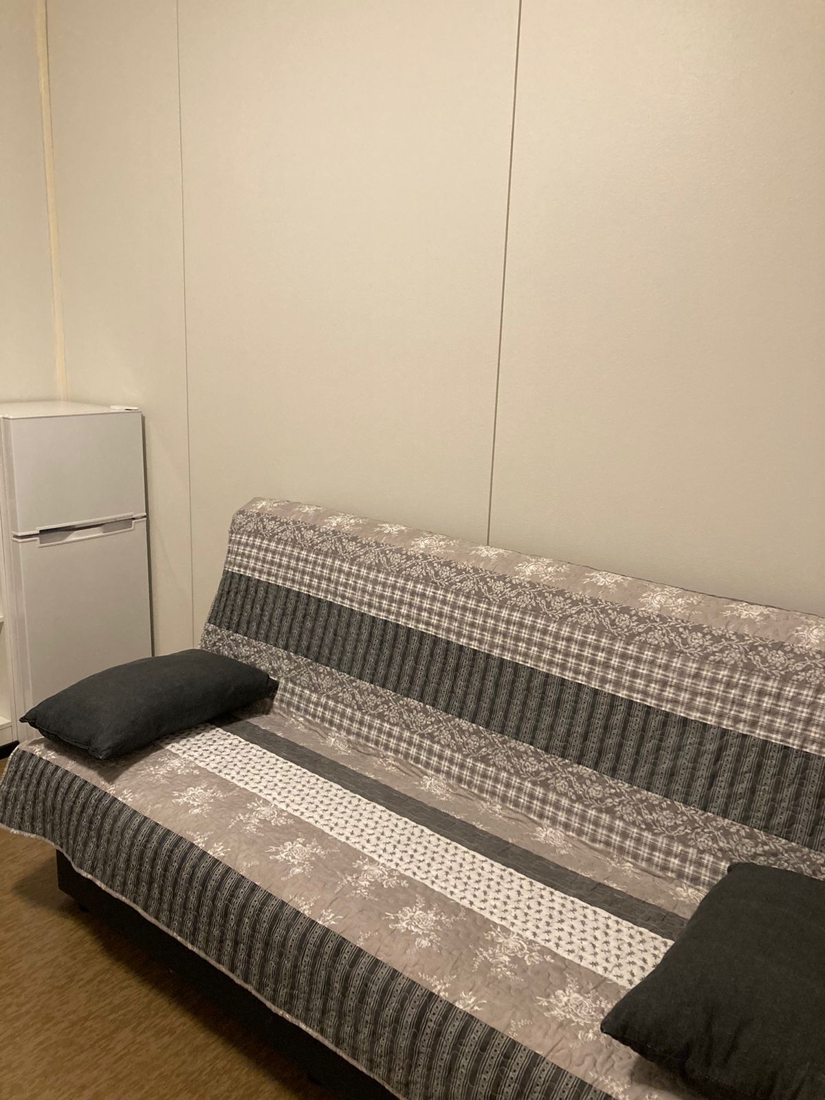 A sofa with a patterned fabric, two black cushions, and a white appliance in the corner.