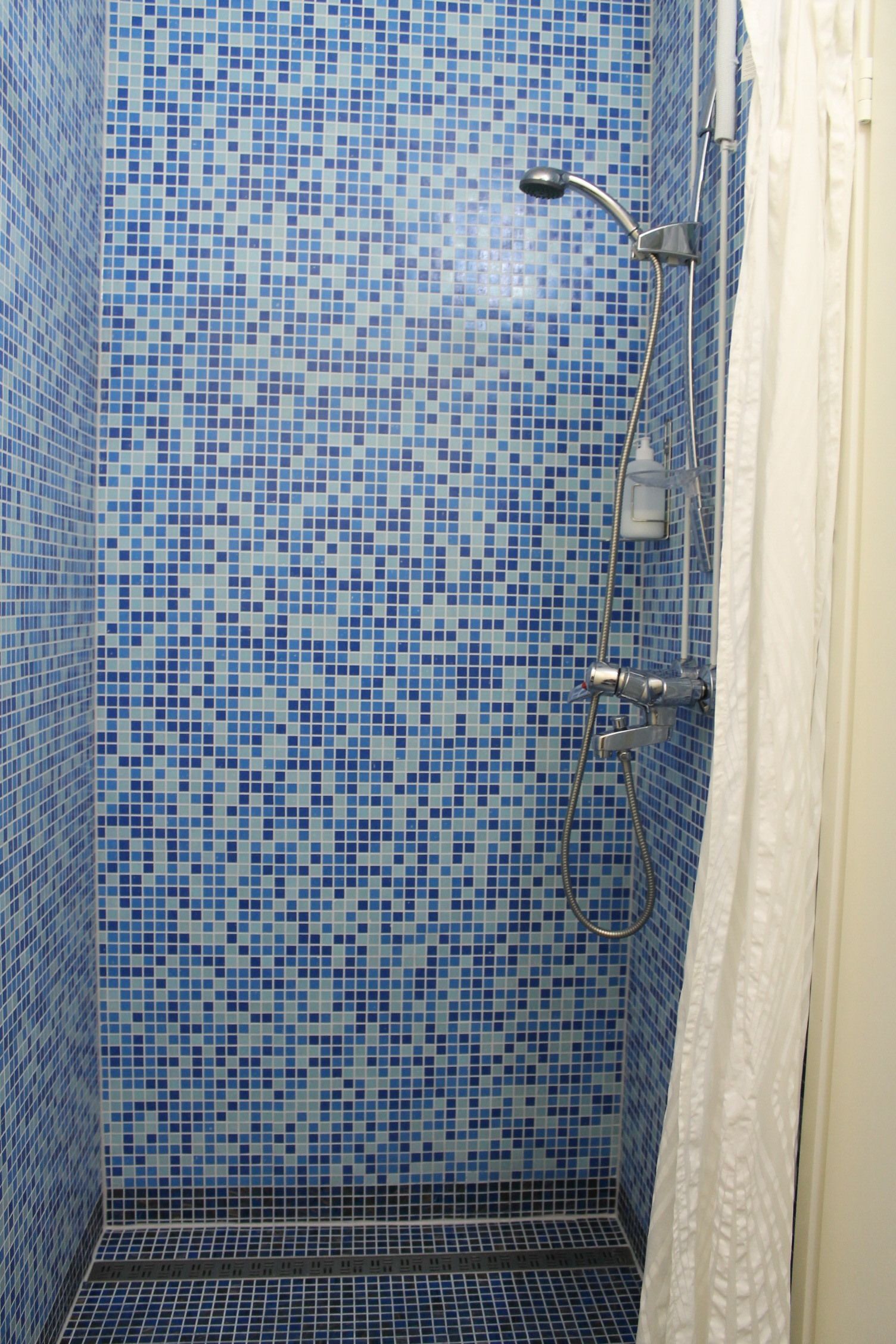 A bathroom with blue mosaic tile walls and floor, a shower with a handheld showerhead, and a white shower curtain.