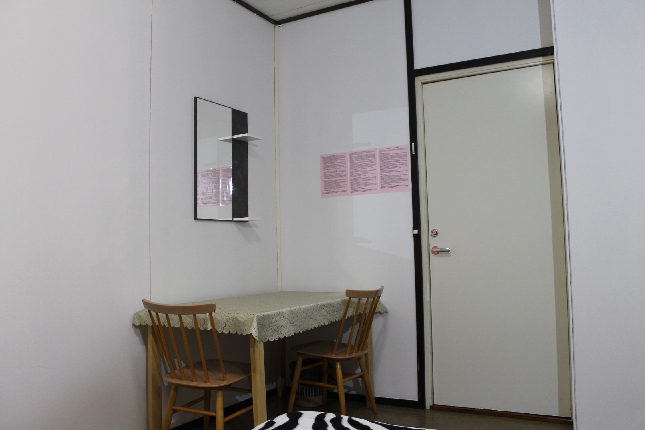 Une petite pièce avec une seule table et deux chaises, une porte et un miroir fixé au mur.