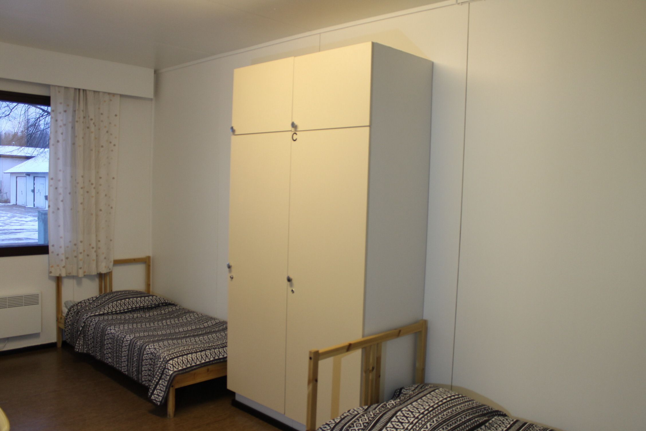 Un dormitorio con dos camas individuales, un armario y una ventana con cortinas.