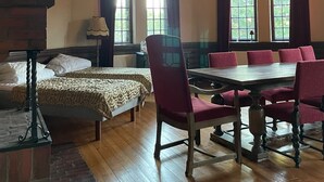 Una habitación con techo de madera, chimenea, una mesa de comedor con sillas y una cama con colcha estampada.