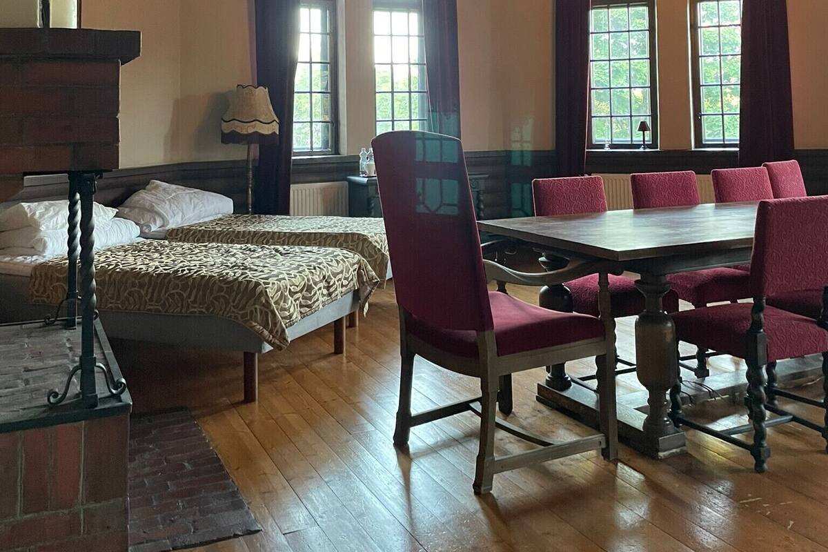 A room with a wooden ceiling, a fireplace, a dining table with chairs, and a bed with a patterned bedspread.