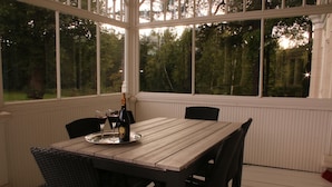 Una mesa de madera con sillas en un espacio exterior cubierto con ventanas grandes.