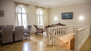 Una habitación amplia con piso de madera, un comedor con sillas, una escalera con barandal blanco y un cuadro en la pared.