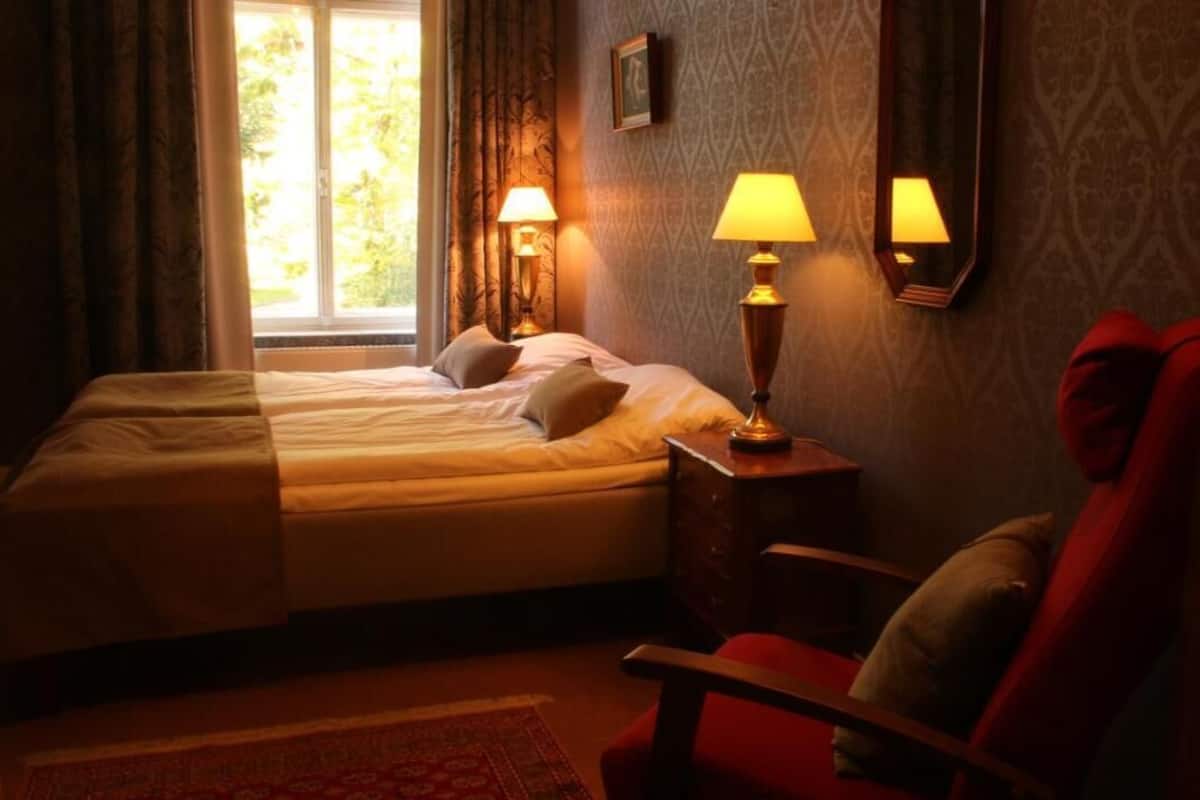 A hotel room with a bed, two bedside lamps, a chair, and a window with curtains.