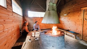 A wooden cabin interior with a stone fireplace, wooden benches, and a high ceiling.