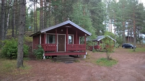 A small cabin with a porch and a door, surrounded by trees and a dirt path.
