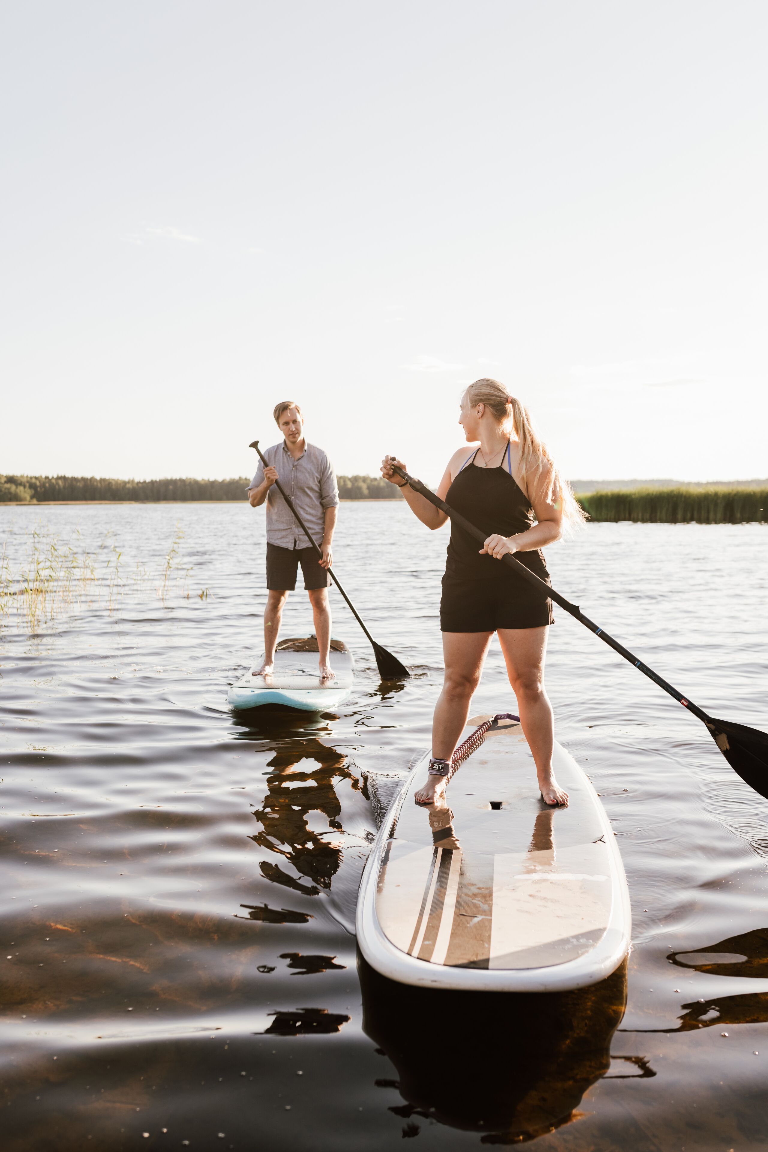 Deux personnes pratiquent le paddle sur un lac calme, sous un ciel dégagé.