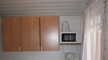 A compact kitchen with wooden cabinets, a microwave, a coffee maker, and a small refrigerator.