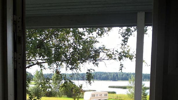 A covered outdoor area with a table and two chairs, overlooking a lake and a grassy field.