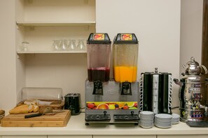 A breakfast bar with a juice dispenser, a coffee machine, and a bread basket.