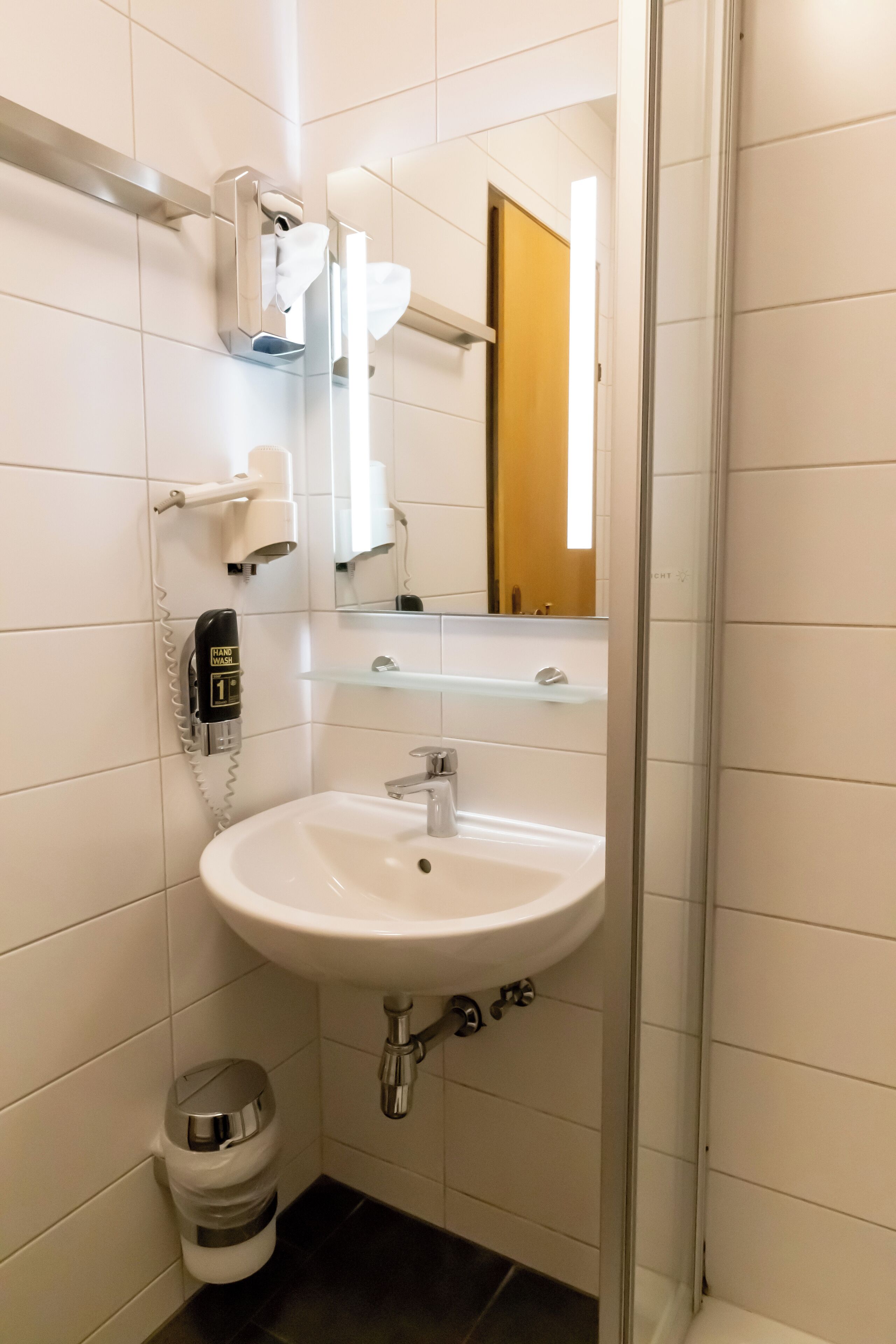 A bathroom with a white sink, a mirror, a hairdryer, and a trash bin.