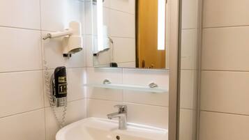 A bathroom with a white sink, a mirror, a hairdryer, and a trash bin.