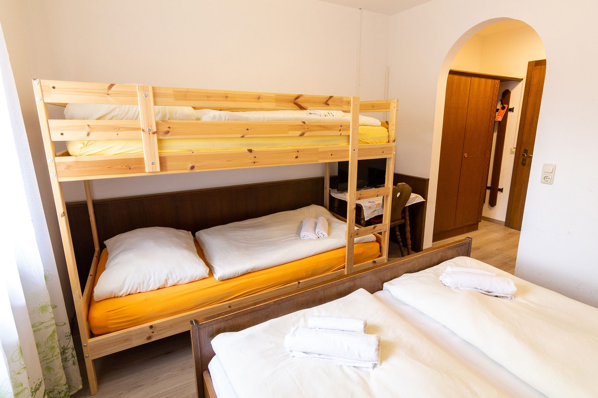 Habitación con literas, dos camas bajas y una litera superior. Se observa un armario de madera y una silla en la esquina.