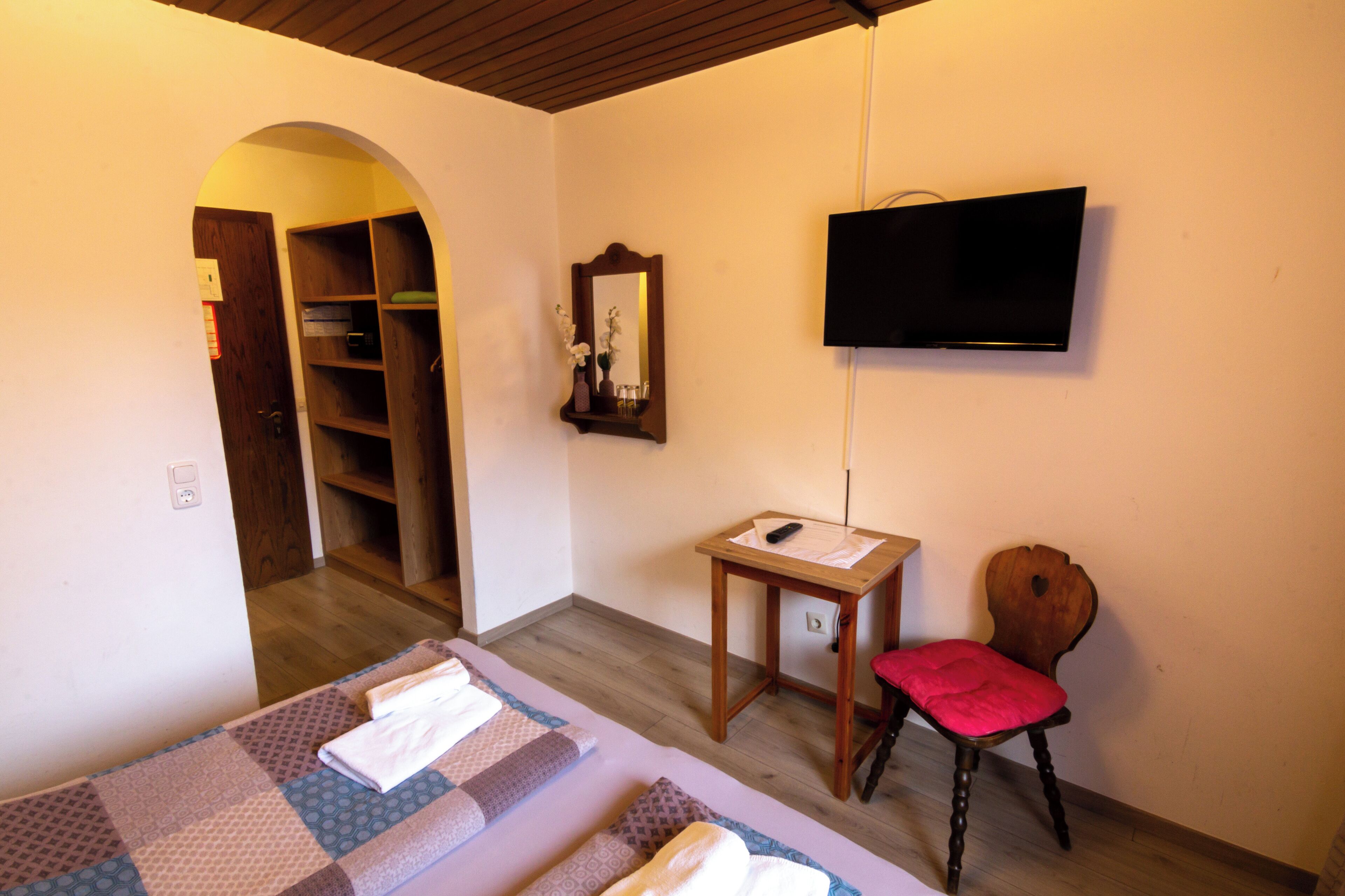A room with a bed, a chair, a TV, a mirror, and a wooden cabinet.