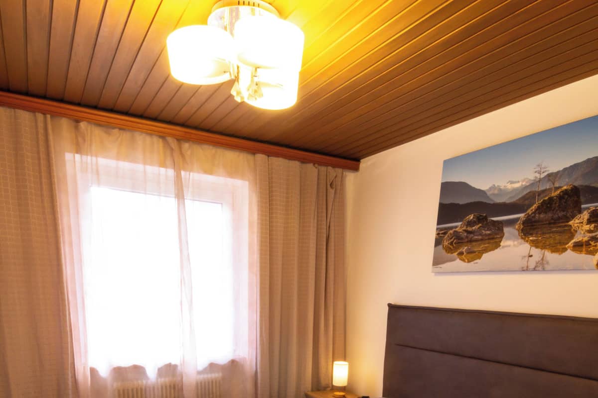Un lit double avec une tête de lit en bois, une table de chevet avec une lampe et une fenêtre ornée de rideaux légers.