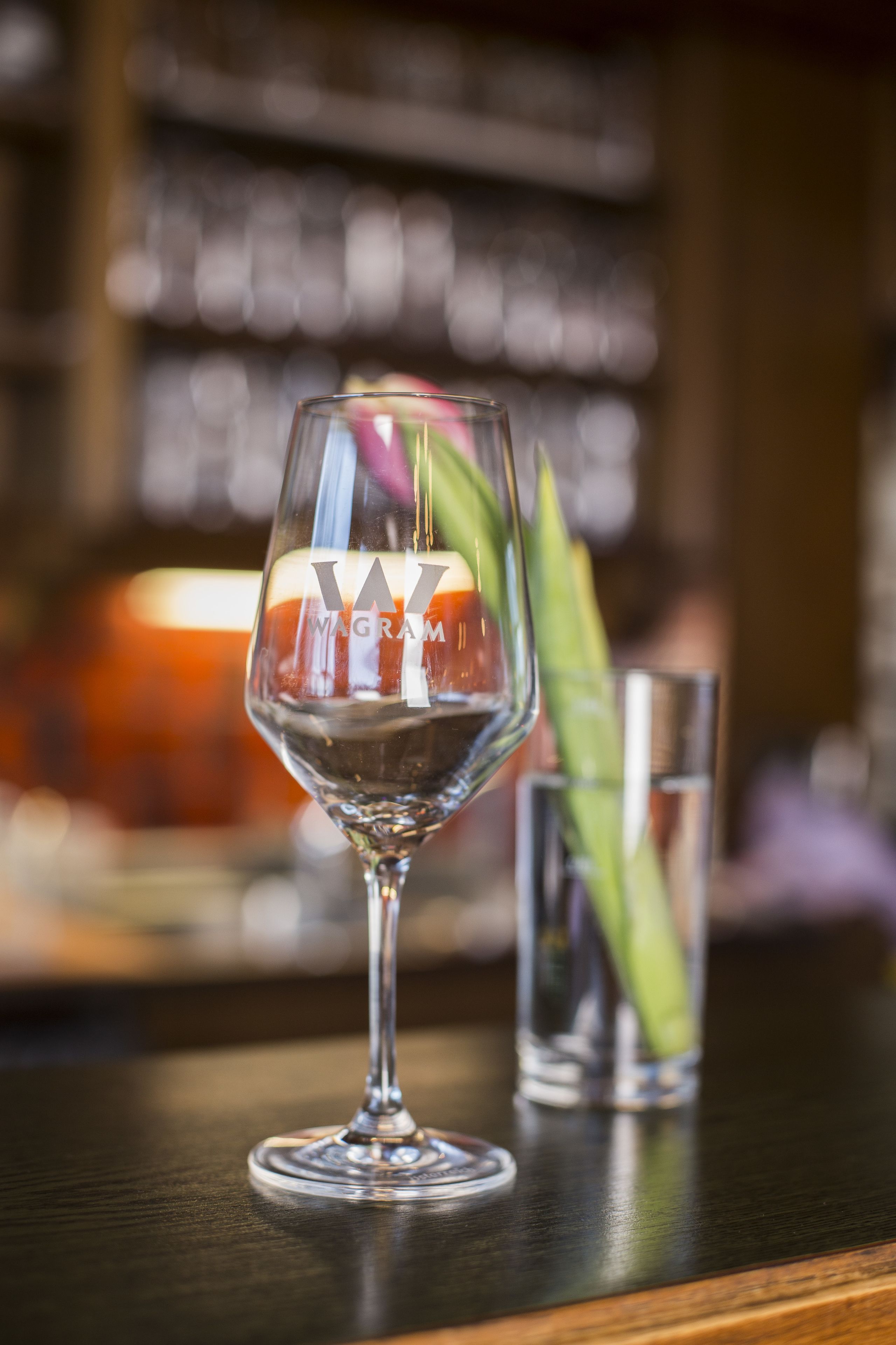 A bar setting with a glass of red wine and a green garnish on a wooden bar counter.