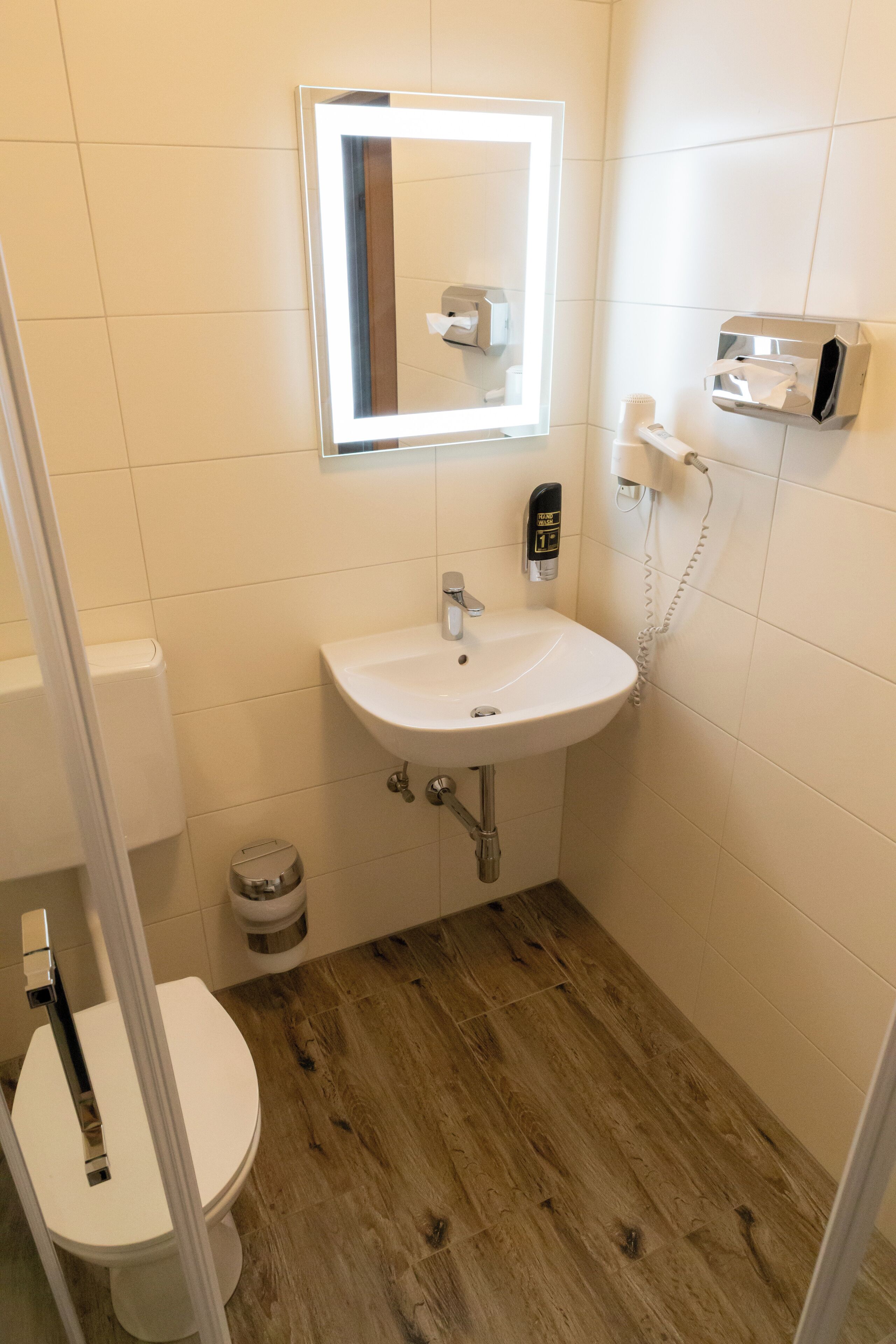 A bathroom with a white sink, a mirror, a toilet, and a trash can.