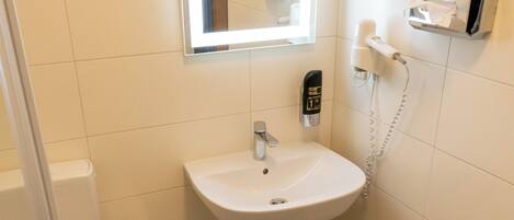 Une salle de bain avec un lavabo blanc, un miroir, des toilettes et une poubelle.