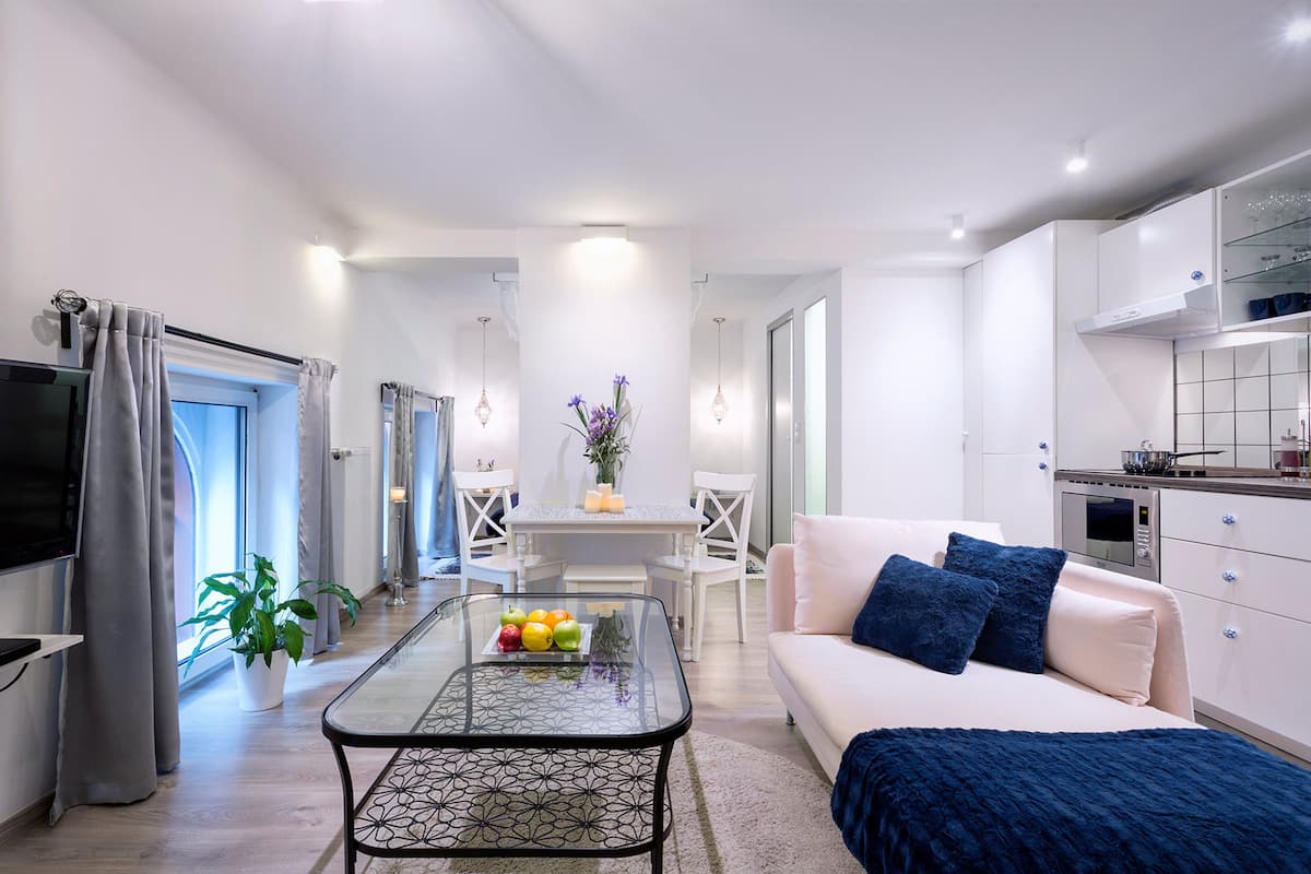 Una sala de estar moderna con un sofá, una mesa de centro con fruta, un televisor y una zona de cocina con armarios y un microondas.