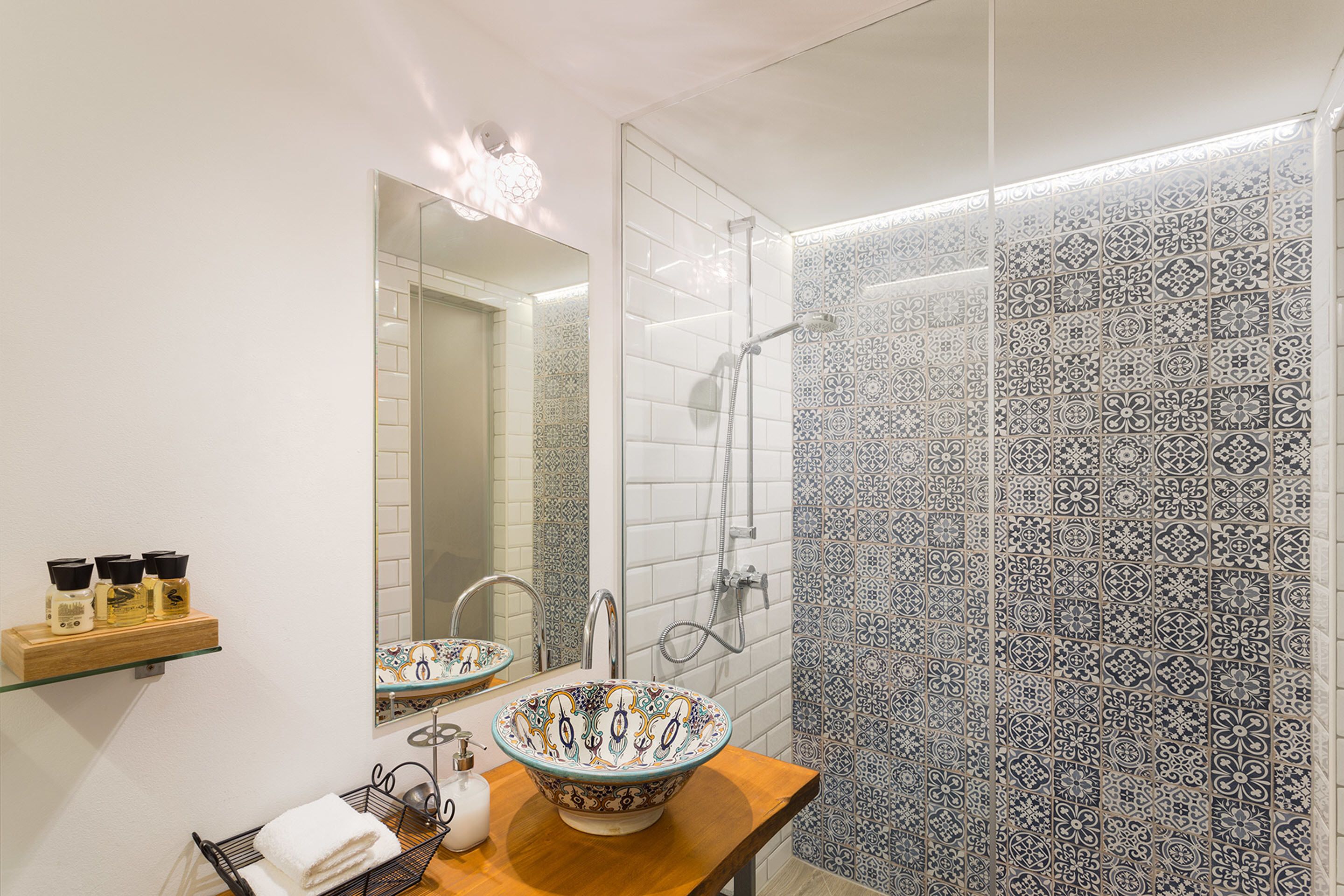 A bathroom with a large mirror, a bowl sink, a shower, and patterned tiles.