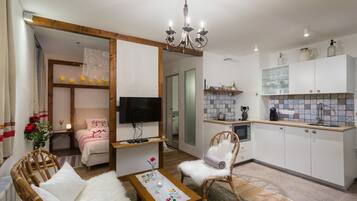 A cozy living room with a television, a sofa, a coffee table, and a dining area with a kitchen in the background.