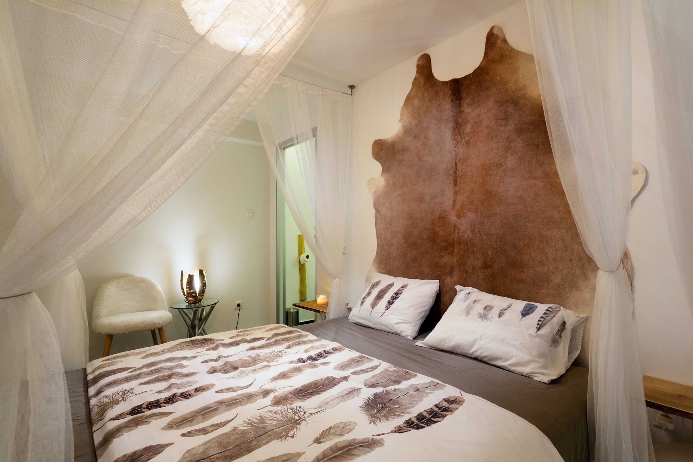 Un dormitorio con una cama grande, un cabecero de cuero de vaca y cortinas translúcidas.