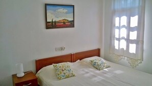 Ein Schlafzimmer mit Bett, zwei Kissen, einem Nachttisch, einer Lampe, einem Bild an der Wand und einem Fenster mit Vorhang.