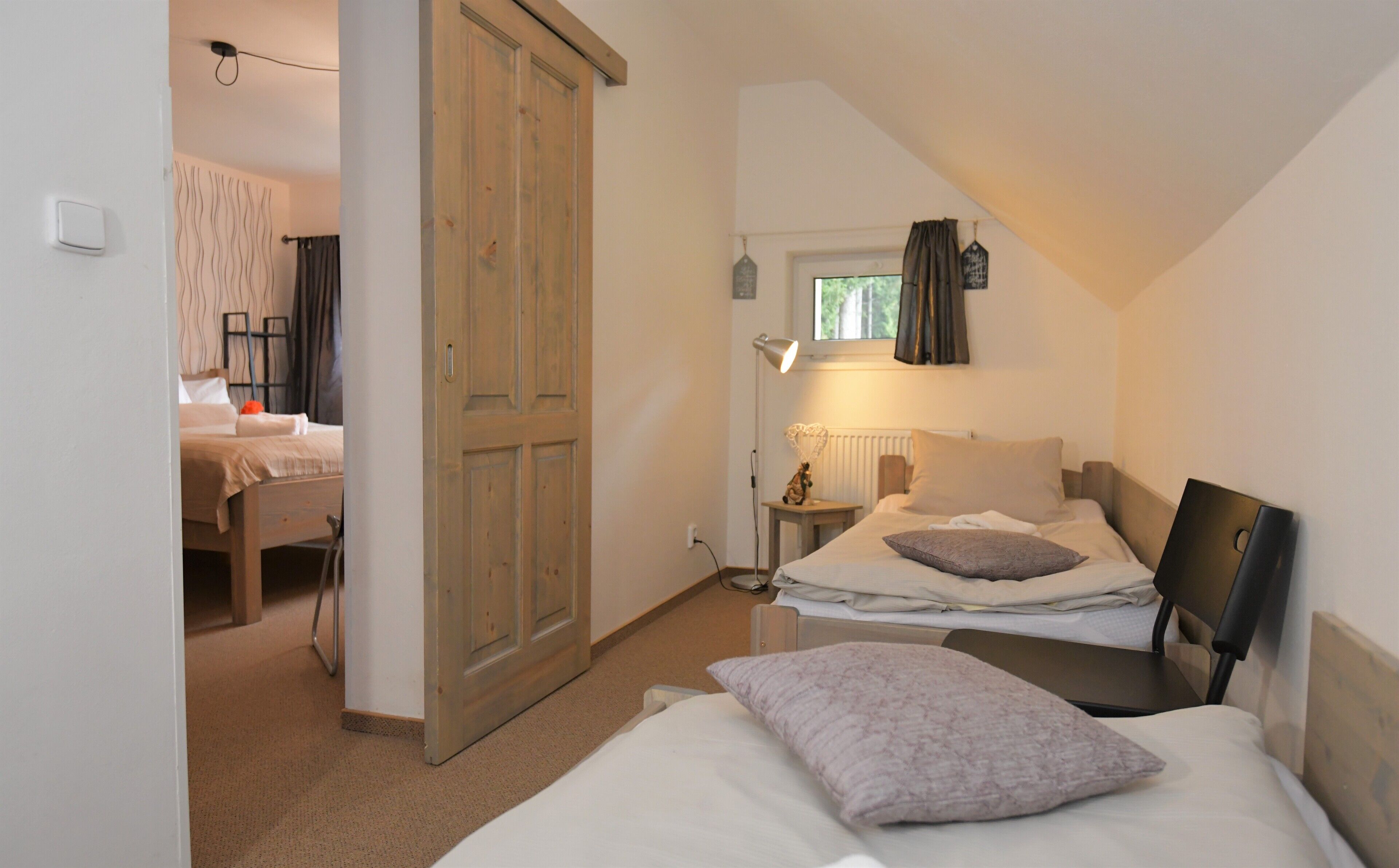 Une chambre avec deux lits, une armoire en bois, une table de chevet avec une lampe et une fenêtre avec des rideaux.