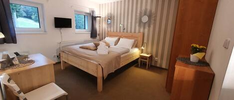 A neatly arranged bedroom with a bed, bedside table, and a desk with a chair.