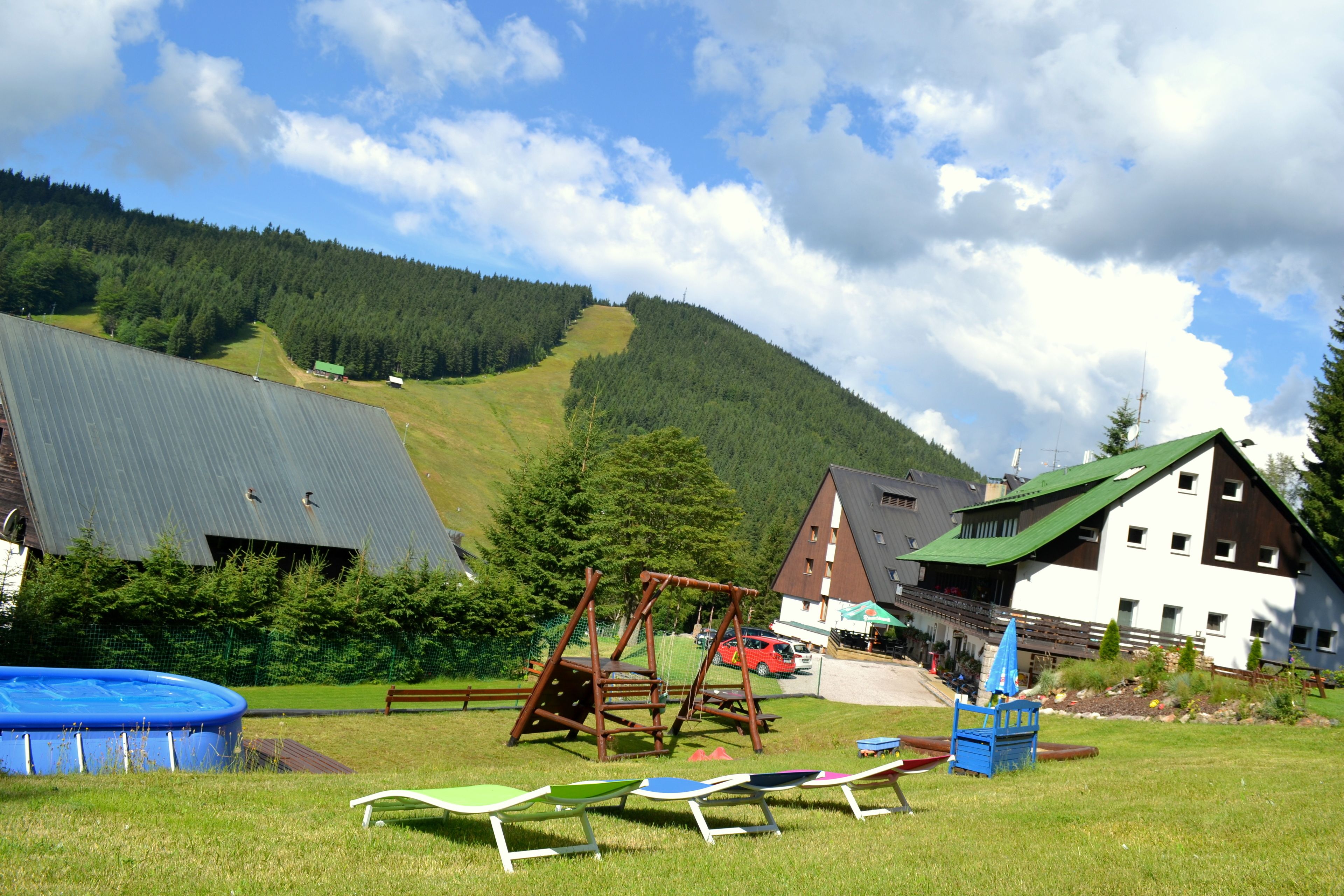 A playground with swings and slides, a blue inflatable pool, and a building with a green roof.