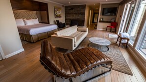 A modern hotel room with a bed, sofa, leather chair, and a small table. - Interlaken Inn & Resort (Lakeville)