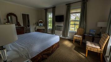 A hotel room with a large bed, a dresser, a chair, a television, and a window with curtains.
