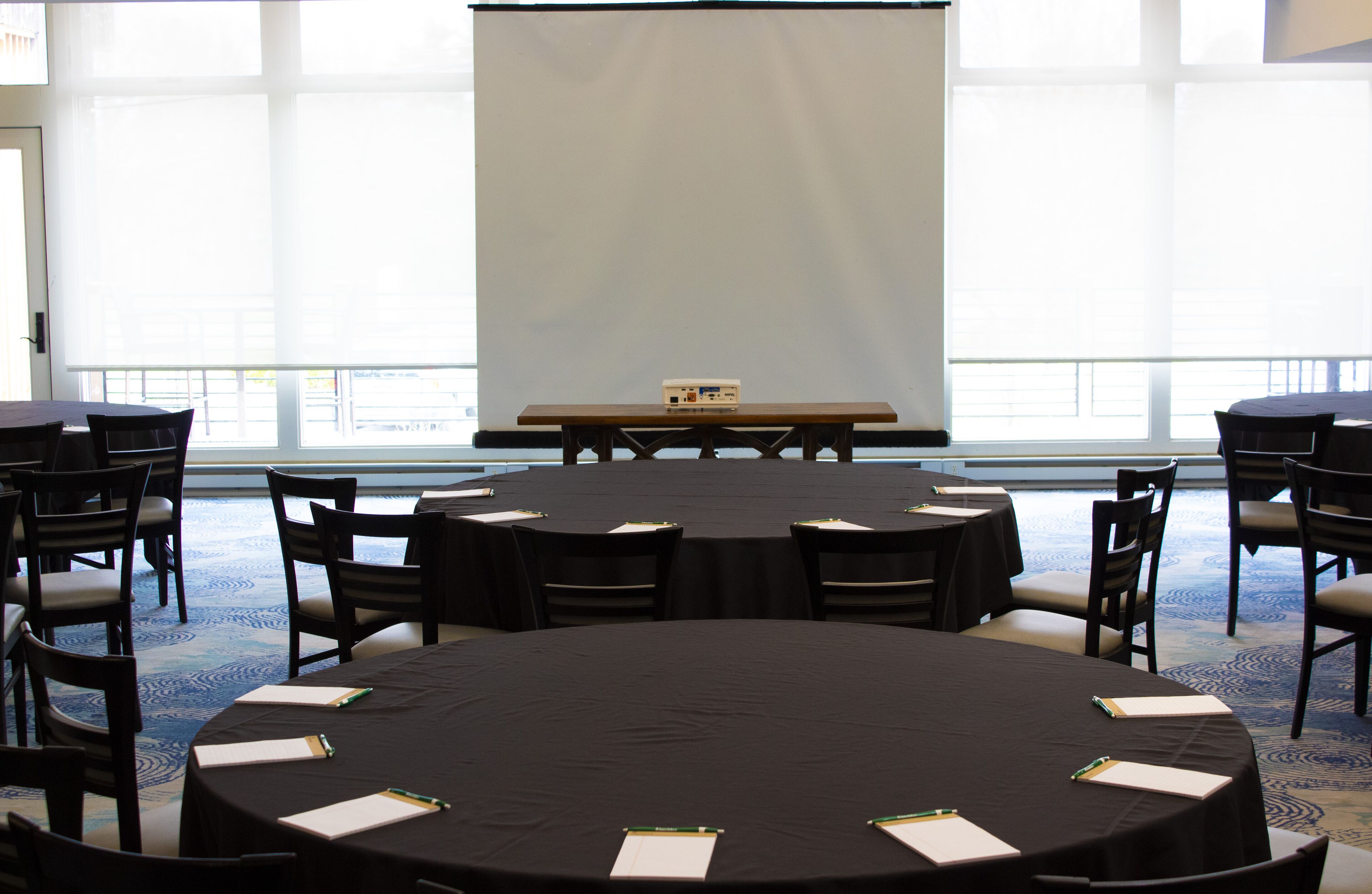 Un salón de conferencias con una pantalla grande, mesas redondas y sillas.