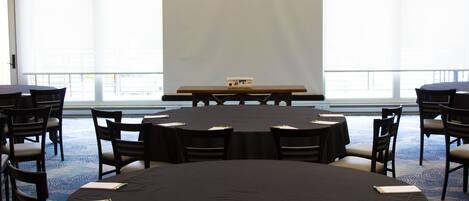 Un salón de conferencias con una pantalla grande, mesas redondas y sillas.