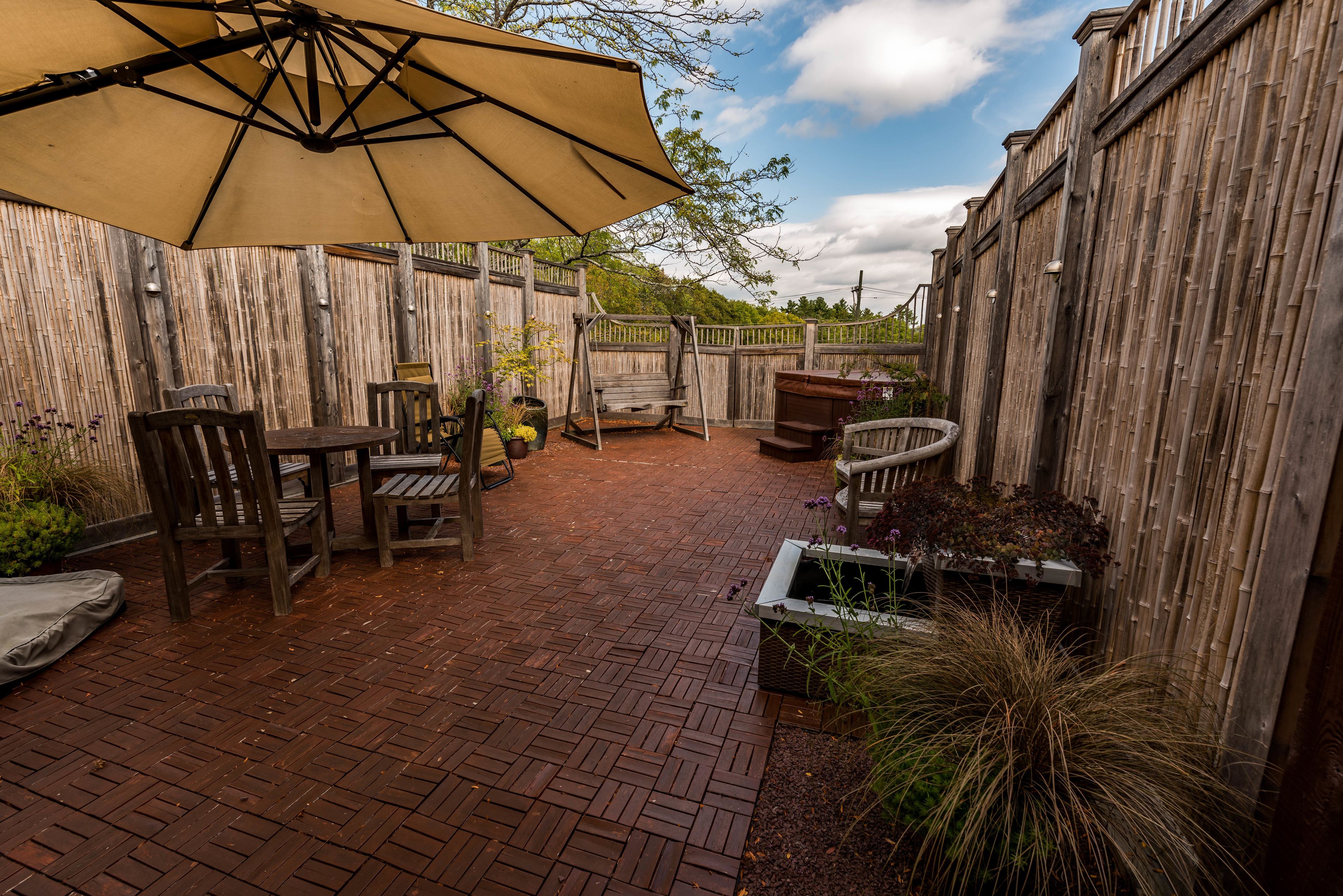 A patio area with a brick floor, wooden furniture, and a large umbrella.